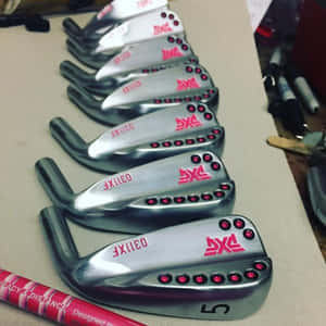 PXG 高爾夫鐵桿帶有紅色點綴，整齊排列在工作台上。 — 高爾夫球場 壁紙
