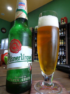 酒吧木製吧檯上的一支綠色Pilsner Urquell啤酒瓶和一杯滿的啤酒。 — 啤酒 壁紙