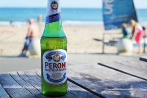 陽光海灘木桌上的綠色 Peroni 啤酒瓶 — 海灘 壁紙