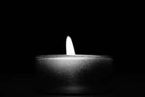 一支在黑暗中發光的點燃蠟燭 — 省電 壁紙