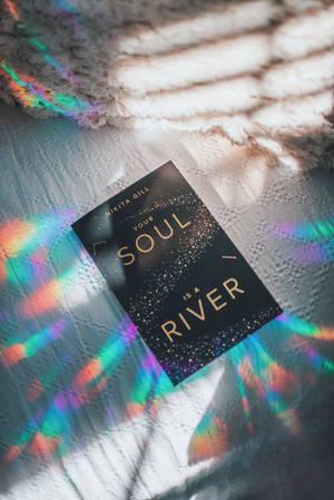 一本名為《Your Soul Is a River》的書放在一個有紋理的表面上，帶有彩色光圖案。 — 書本美學 壁紙