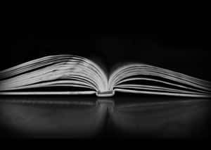 在戲劇性燈光下，深色反光表面上的打開書本，頁面清晰。 — 書本美學 壁紙