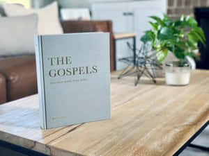 一本灰色書名為 'The Gospels' 的書放在木桌上，附近有植物和蠟燭。 — 教堂 壁紙