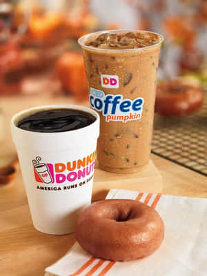 Dunkin' Donuts南瓜冰咖啡和黑咖啡，木桌上有一個糖霜甜甜圈。