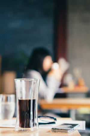 桌上的咖啡杯，背景有一個模糊的人在喝咖啡。 — 咖啡美學 壁紙