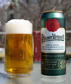 戶外金屬桌上的一杯啤酒和一個 Pilsner Urquell 罐。 — 啤酒 壁紙