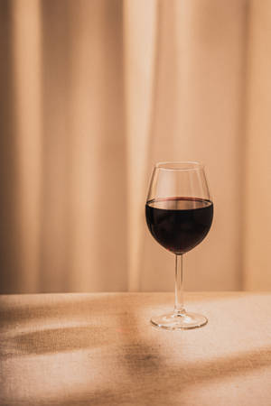 一杯紅酒放在桌上，背景有窗簾。 — 葡萄酒 壁紙