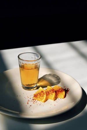 一杯飲料和沾有香料的柑橘片放在盤子上，在強烈陽光下。 — 檸檬 壁紙