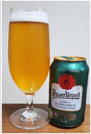 一杯啤酒放在木質表面上，旁邊有一個 Pilsner Urquell 罐。 — 啤酒 壁紙