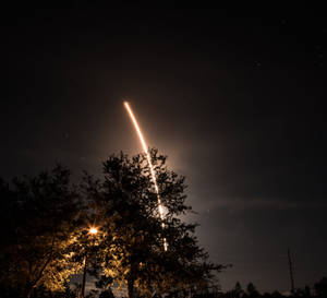 火箭發射到剪影樹木和街燈上方的夜空。 — 光線 壁紙