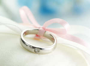 銀色結婚戒指，鑽石和粉紅色絲帶在白色布料上。 — 結婚戒指 壁紙