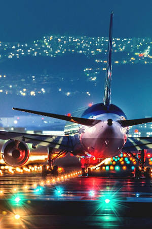 夜間機場跑道，飛機和城市燈光在濕滑的停機坪上反射。 — 伸展台 壁紙