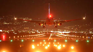 一架飛機在夜間降落，背景有跑道燈光和城市燈光。 — 伸展台 壁紙
