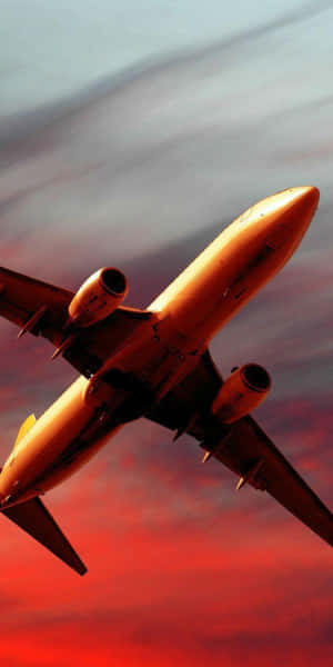 飛機在戲劇性的紅色和橙色日落天空中飛行。 — 18:9 壁紙