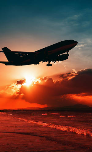 飛機在日落時低飛過海洋，天空呈現鮮豔的橙色，波浪翻湧 — 海灘 iPhone 壁紙