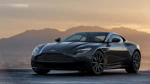 黑色Aston Martin跑車停泊在日落時分有山景的道路上。 — 奧斯頓馬丁 壁紙