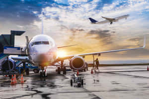 日落時分，一架商用飛機停在機場閘口，另一架飛機正在起飛。 — 航太 壁紙