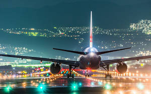 夜間一架大型飛機停在濕滑的跑道上，背景有城市燈光閃爍。 — 伸展台 壁紙