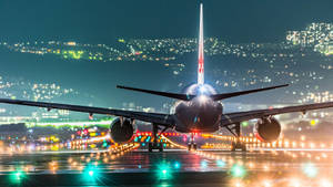 一架大型飛機在夜間停在濕滑的跑道上，背景中城市燈光閃爍。 — 伸展台 壁紙