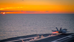 戰鬥機在夕陽下從航空母艦上起飛，背景是海洋 — 伸展台 壁紙