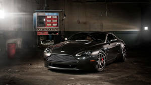 啞光黑色Aston Martin在昏暗的工業車庫中，聚光燈照射。 — 奧斯頓馬丁 壁紙