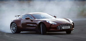 棕色 Aston Martin 在賽道上飄移，身後留下濃煙。 — 奧斯頓馬丁 壁紙