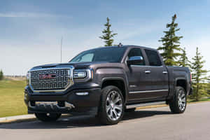 深灰色 GMC Sierra Denali 貨卡停在有樹木和草地的道路上。 — Gmc 壁紙
