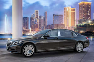 豪華 Mercedes-Maybach S-Class 轎車停泊在黃昏時分發光的城市天際線前。 — 好看汽車 壁紙