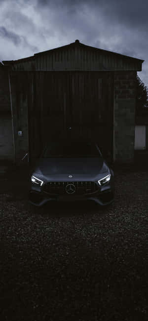 深灰色 Mercedes-AMG 停放在風雨交加的天空下的一座質樸穀倉前。 — Galaxy M36 壁紙