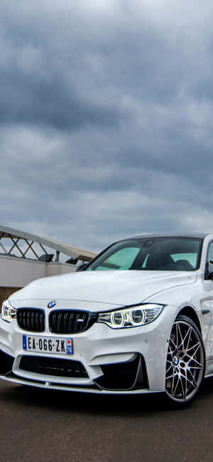 白色BMW M4跑車在戶外多雲天空下停放，靠近現代建築。 — Redmi Note 13 Pro 壁紙