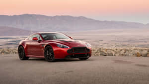 紅色Aston Martin跑車停放在日落時分的山景觀景點上。 — 奧斯頓馬丁 壁紙