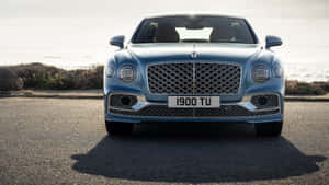 藍色 Bentley Bentayga 停泊在日落時分靠近海洋的沿海道路上。 — 低調 壁紙