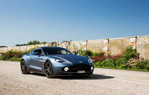 藍色Aston Martin跑車停放在碎石上，靠近花園和磚牆。 — 阿斯頓維拉 壁紙