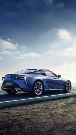 藍色Lexus LC 500在日落時分沿海岸高速公路飛馳。 — 美學藍色 iPhone 壁紙