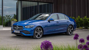 藍色賓士轎車停放在現代建築物附近，伴有紫色花朵。 — Mercedes Benz C300 壁紙