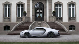 銀色 Bugatti Chiron 停泊在一座宏偉的石砌大宅前，配有拱形窗戶和對稱樓梯。 — 布加迪 GIF 壁紙