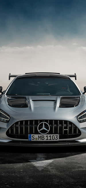 在暴風雨的天空下，潮濕道路上的銀色 Mercedes-AMG GT R 跑車。 — iPhone 16 Pro Max 壁紙