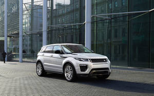 銀色 Range Rover Evoque 停放在玻璃建築前，附近有行人走過。 — 高清 壁紙