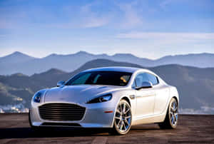 銀色Aston Martin跑車停泊在日落時分的山景觀景點。 — 奧斯頓馬丁 壁紙