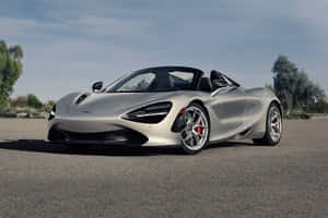 銀色McLaren 720S Spider敞篷跑車停在鋪砌的道路上，有樹木和天空。 — 麥拉倫 壁紙