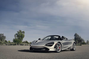銀色McLaren 720S Spider敞篷跑車停放在開闊的道路上，背景有樹木和天空。