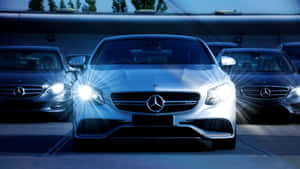夜晚一排豪華汽車中，銀色梅賽德斯轎車配以明亮的車頭燈。 — Mercedes Benz C300 壁紙
