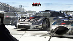 銀色賽車在賽道上奔馳，背景可見其他車輛和贊助商標誌。 — 賽車計畫 壁紙