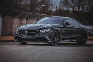 黑色Brabus Mercedes-AMG S 65 Coupe停泊在帶刺鐵絲網圍欄附近。 — 高清 壁紙