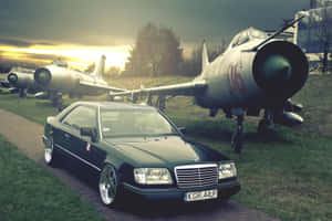 黑色賓士轎跑車停在展示的戰鬥機附近，夕陽時分。 — Mercedes Benz C300 壁紙