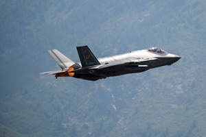 F-35戰鬥機在森林覆蓋的山脈上空飛行，後燃器啟動。 — 空軍 壁紙