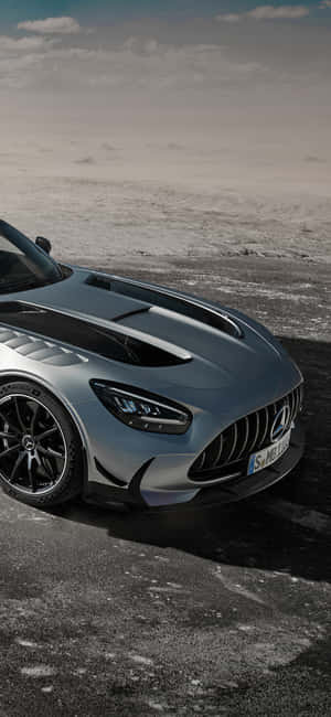 銀色 Mercedes-AMG GT R 跑車在積雪路上，多雲天空。 — iPhone 16 Pro 壁紙