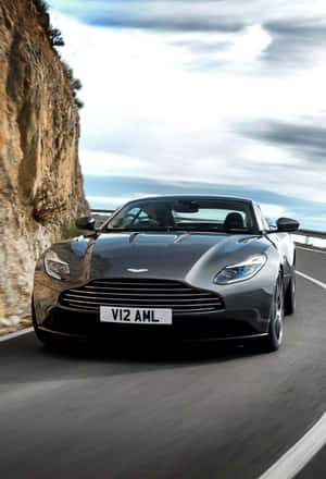 銀色Aston Martin V12敞篷跑車在懸崖附近的海岸公路上奔馳。 — iPhone Duo 壁紙