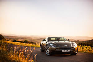 夕陽下風景如畫的鄉村道路上的銀色Aston Martin DB11。 — 奧斯頓馬丁 壁紙