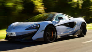 銀色McLaren跑車在陽光明媚的道路上與綠色樹木一起奔馳。 — 麥拉倫 壁紙